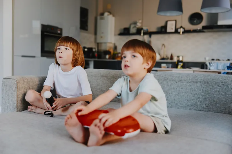 Two young boys focused on playing video games together, showcasing excitement and concentration in a cozy living room setting. A perfect capture of childhood fun.