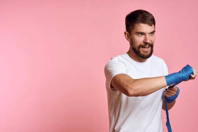 Спортивный мужчина в белой футболке с боксёрскими бинтами на руках, тренировка, образ жизни, розовый фон