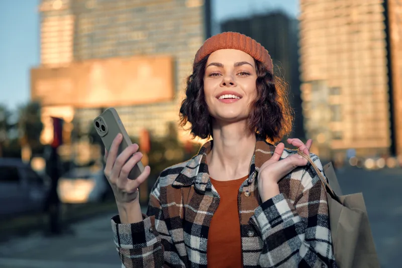 woman smile urban golden hour phone shopping candid lifestyle beanie happiness. Authentic candid lifestyle portrait of a young woman holding phone and shopping bag in golden hour glow, mindful living.