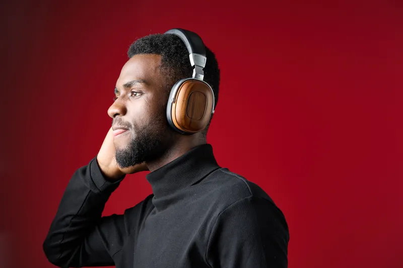 A stylish young black man wearing headphones, enjoying music against a vibrant red background, showcasing confidence and modern aesthetics