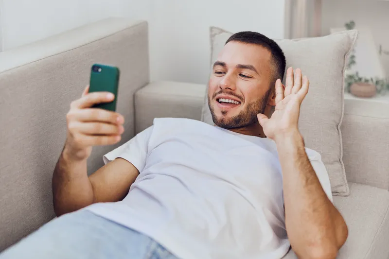 Friendly man enjoying a video call at home, wearing a casual t-shirt. His relaxed posture and cheerful smile create an inviting atmosphere for virtual connection.