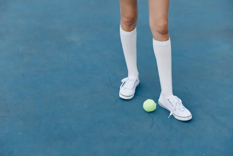 Young female athlete in white socks and sneakers on a blue tennis court, showcasing determination and focus while preparing for a game