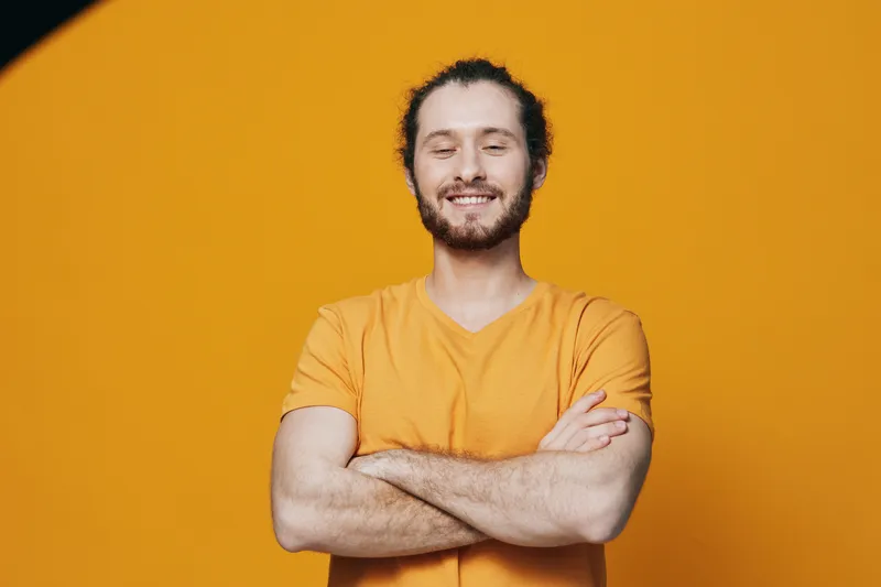 Smiling young man in a yellow shirt against a vibrant orange background, expressing confidence and warmth, suitable for personal branding and positivity concepts