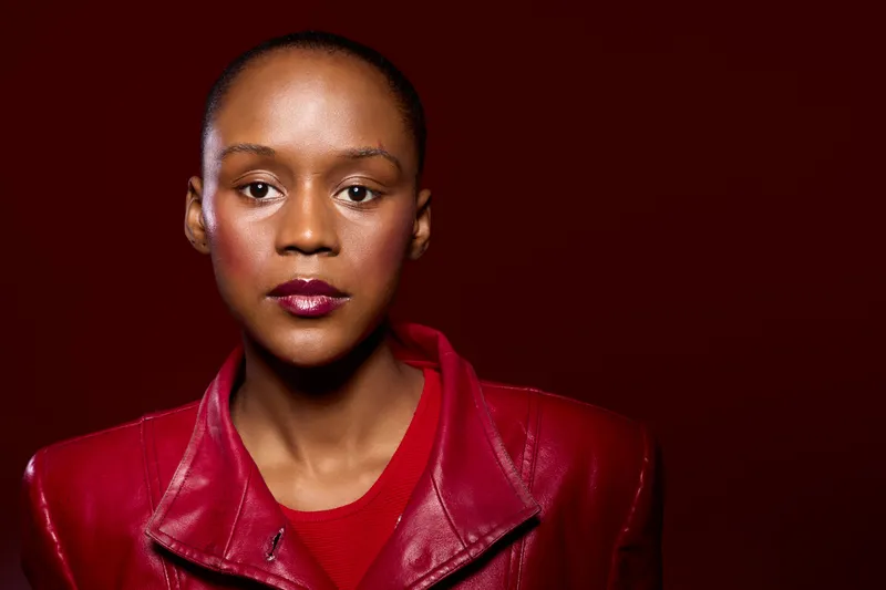 Portrait of confident black woman with dark skin wearing red leather jacket and red shirt. Studio shot on dark red background. Concept of fashion, style, and beauty with ethnic focus.