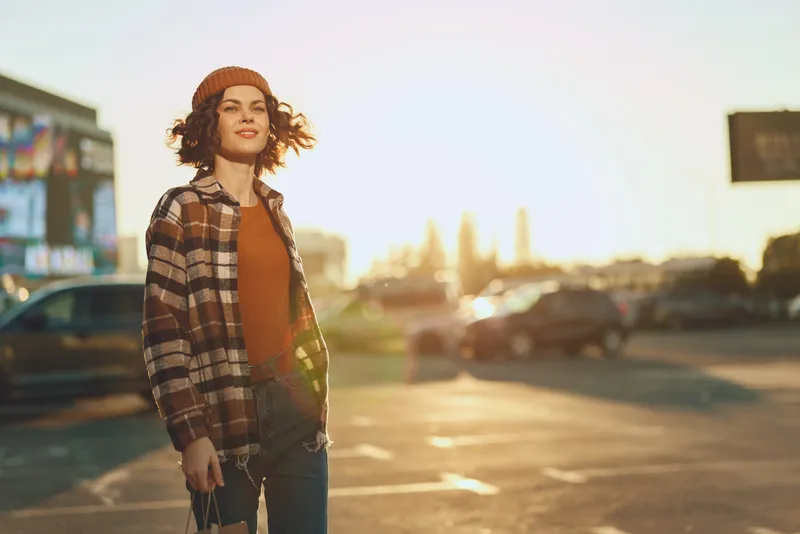 woman walking street urban golden candid portrait in golden hour glow, smiling young adult in plaid jacket and beanie, authenticity and mindful living captured in emotional storytelling