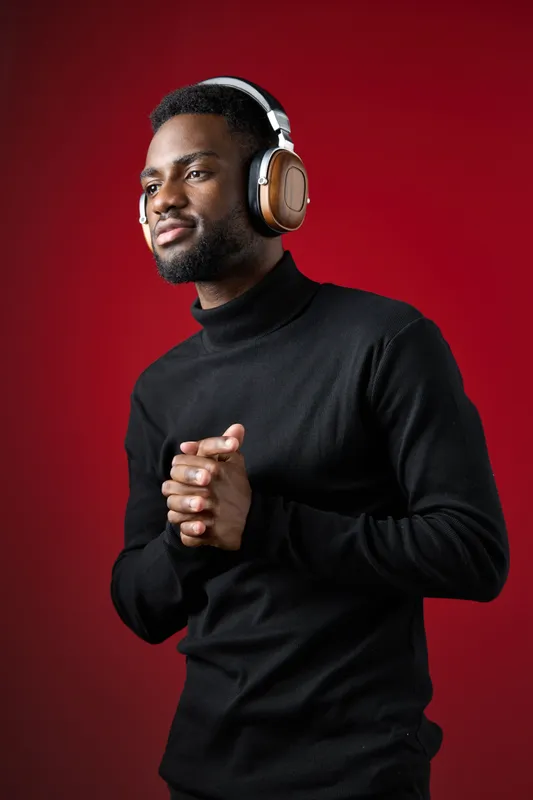 Thoughtful Black man enjoying music with headphones in a stylish black turtleneck against a vibrant red background