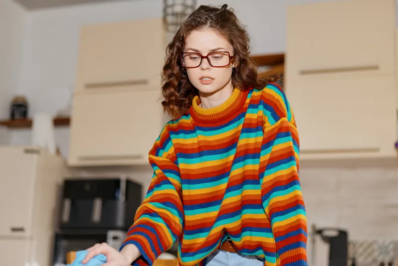 A woman wearing a colorful striped sweater engages in a home kitchen task, capturing a candid lifestyle moment in a bright, contemporary setting, emphasizing everyday home life and personal style.