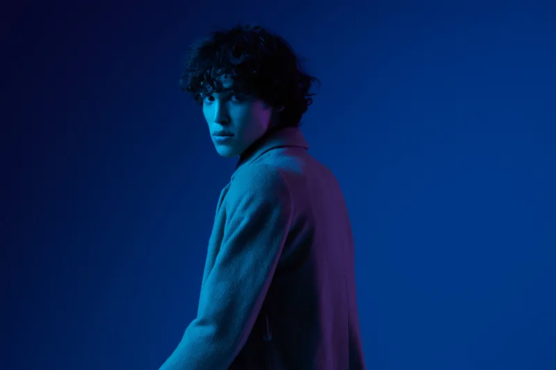 Мужчина-модель в модном пальто на темно-синем фоне, неоновый свет, стиль и тренды, смешанный свет, мужская мода, есть место для копирования