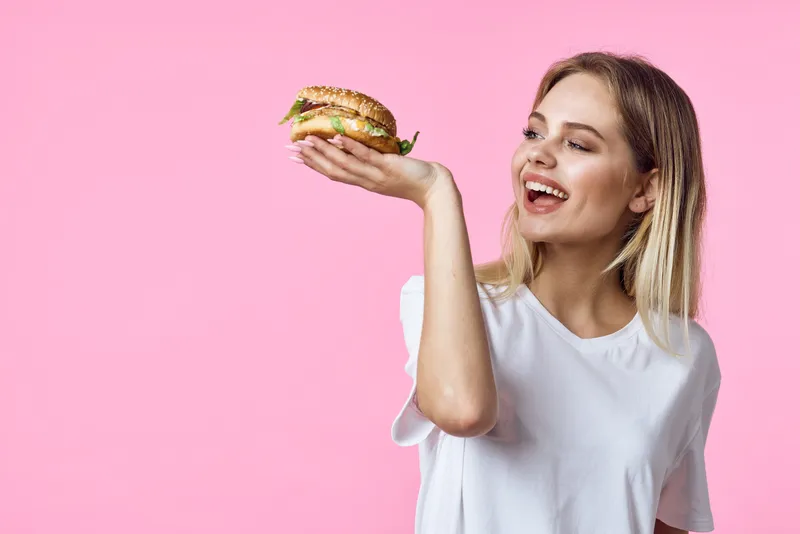 Милая блондинка в белой футболке держит гамбургер в ресторане с вкусной едой