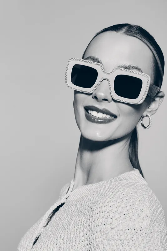 Smiling young white woman with pale skin wearing large stylish sunglasses and hoop earrings in studio. Concept for fashion accessories and modern lifestyle.