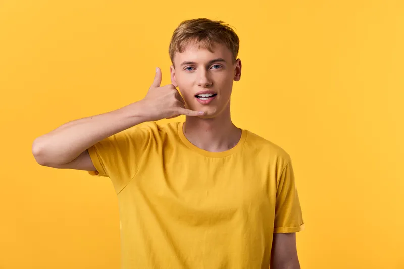 Hand gesture, young man, yellow background, communication, casual, phone gesture, expression, urban, smiling, modern lifestyle, fashion, youth, contemporary energy, marketing vibe