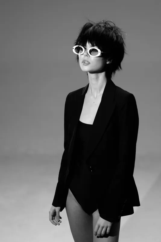 Stylish woman in black blazer and sunglasses posing confidently in black and white image