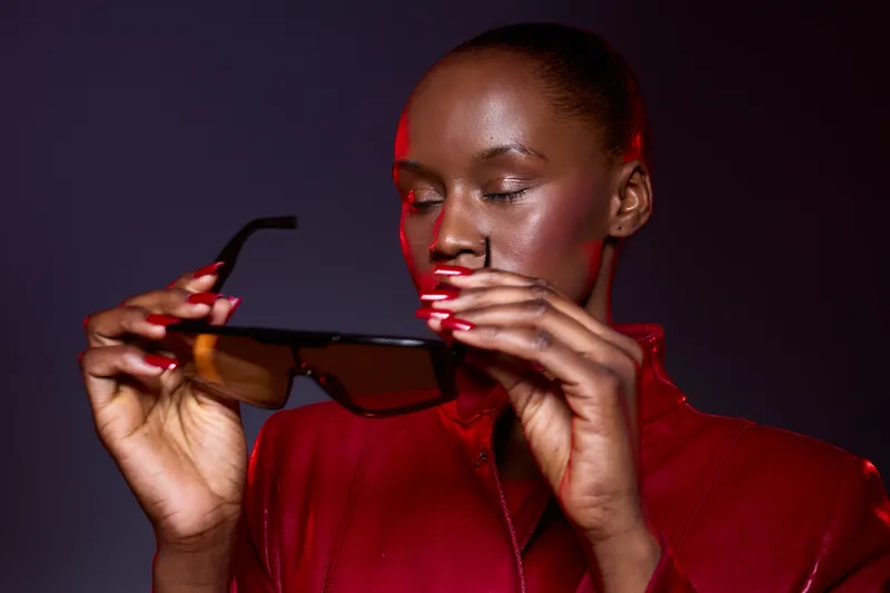 Portrait of a dark skinned African woman wearing a red leather jacket holding black sunglasses. Studio shot with dramatic lighting, concept for fashion, style, and confidence.