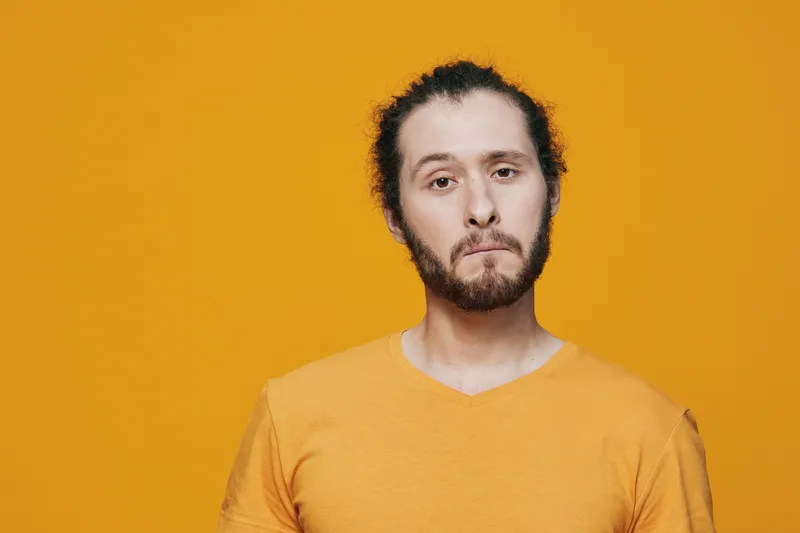 A man with a sad expression in a bright yellow shirt against a vibrant yellow background, symbolizing emotions related to disappointment or sadness