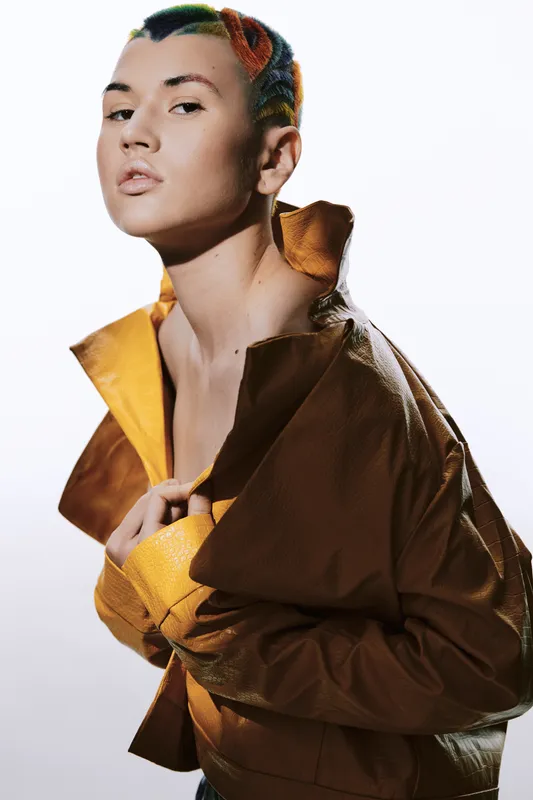 stylish woman with short colorful hair wearing yellow jacket, posing confidently against white background, modern fashion and edgy look