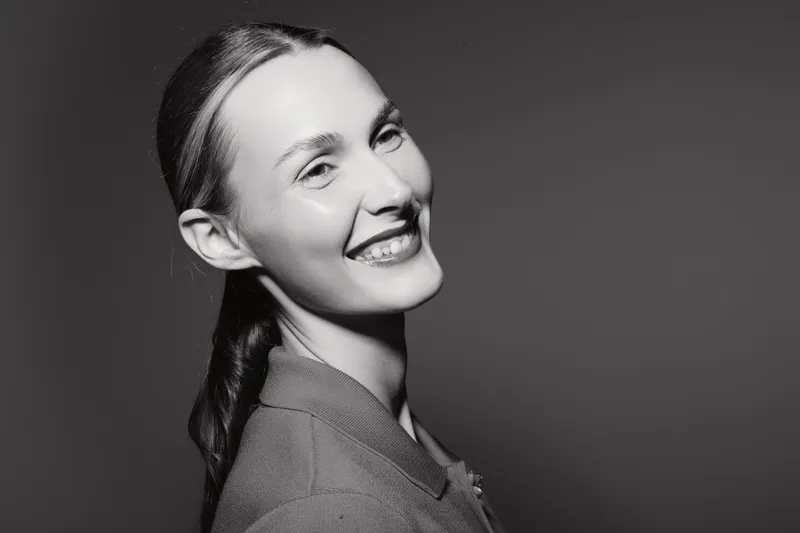 Smiling Caucasian woman with light skin and hair looks at camera in black and white portrait with soft lighting and confident expression.