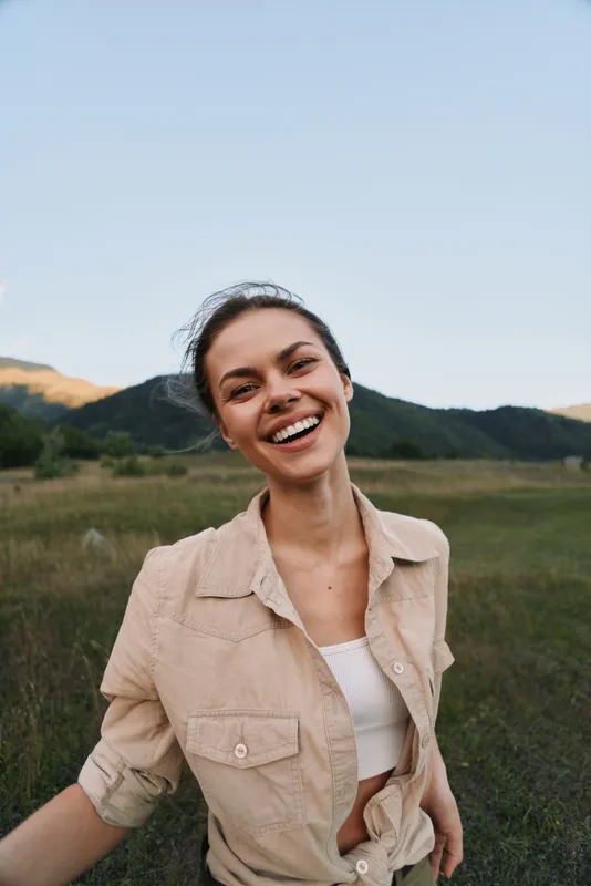 Woman lifestyle portrait outdoors, smiling in casual beige shirt, sunny day in an open field, natural happiness and carefree mood, warm light enhances authentic vibe.