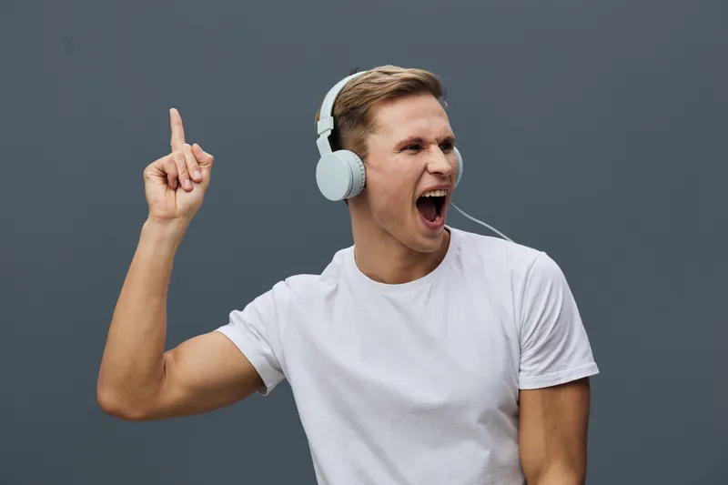 excited young man wearing white headphones listen music enjoy digital detox isolated on gray background casual style lifestyle concept