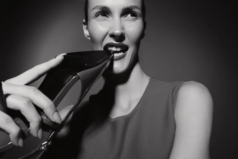 Caucasian woman with light skin biting high heel shoe in black and white photo. Concept of fashion, style, and attitude.