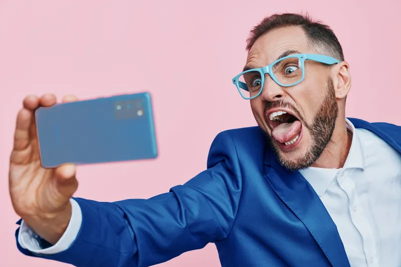 A professional man in a blue suit takes a dynamic selfie against a solid colored background, showcasing confidence, excitement, and focus.