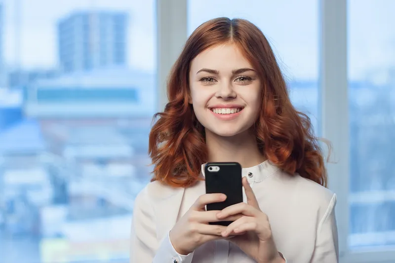 Женщина в рубашке с телефоном в руке; технологии, профессионализм
