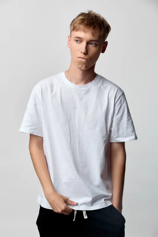 Youth wearing a plain white t shirt and dark shorts stands in a studio, relaxed pose with hands in pockets, casual style and soft lighting for fashion and lifestyle use