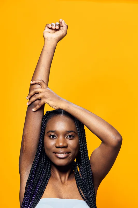Smiling woman with braided hair posing against a vibrant yellow background, showcasing confidence and joy in a stylish outfit