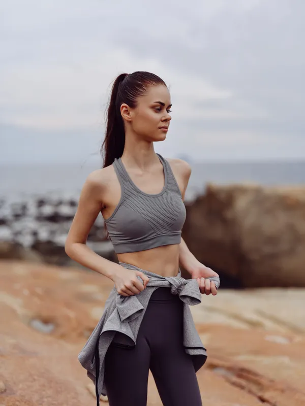 Fit young woman in athletic clothing practicing mindfulness by the sea, showcasing active lifestyle, health awareness, and summer vibes