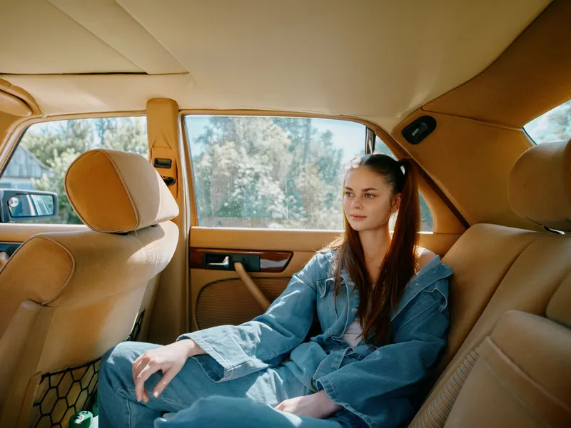 Young woman in denim clothing sitting in a vintage car interior, conveying a relaxed emotion while enjoying a sunny day.