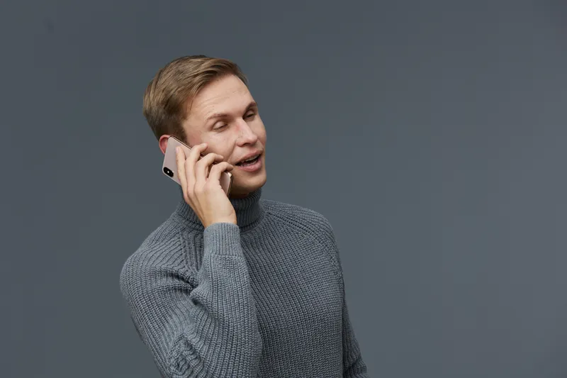 Man talking on mobile phone wearing gray sweater isolated on plain solid gray background studio portrait. People lifestyle concept