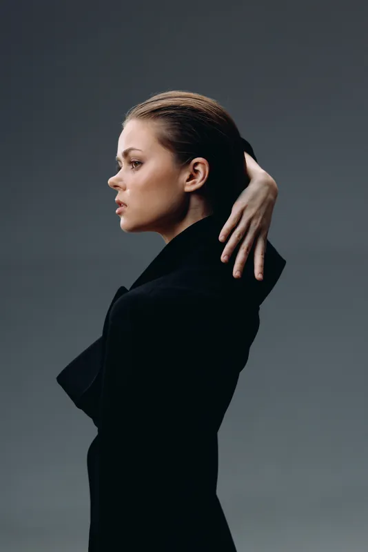 Elegant woman in black coat with thoughtful expression on gray background, minimalistic style, soft lighting, autumn concept