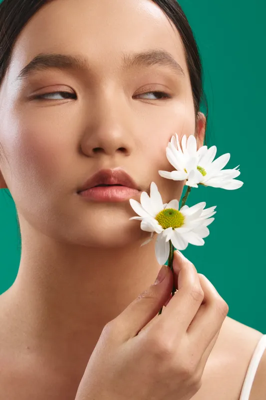 asian woman with delicate flowers near her face in a soft studio setup, serene expression and gentle makeup, creating a calm and elegant beauty portrait.