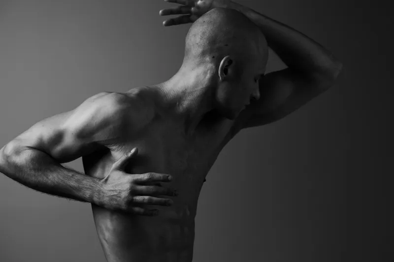 Black and white image of a strong man in an artistic pose, showcasing muscular definition and emotion. The composition creates a powerful visual impact.