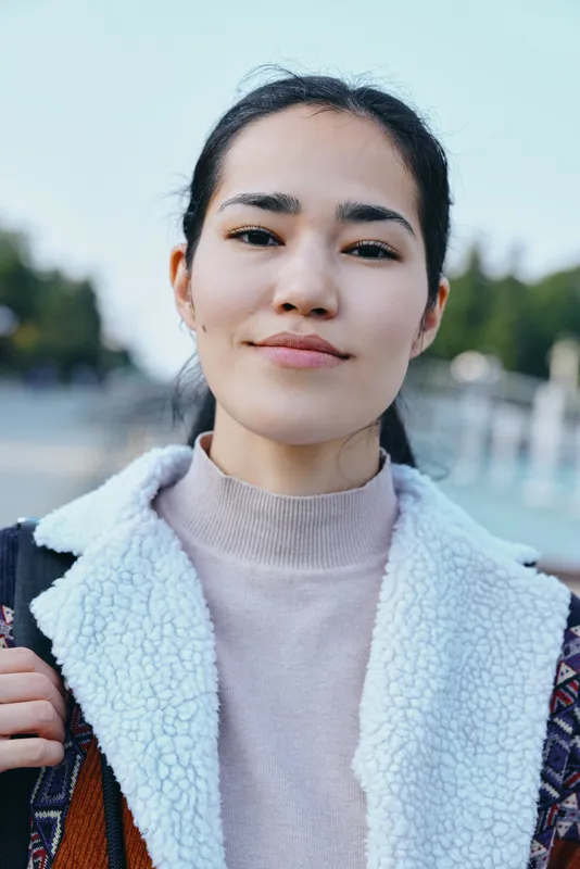 Woman outdoors wearing a light fleece jacket with a soft collar, calm expression, blurred trees in background, casual style for lifestyle, fashion and everyday confidence in natural light