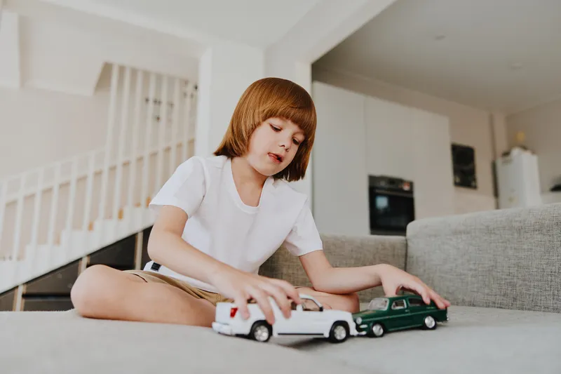 Young boy playing with toy cars, enjoying a sunny afternoon indoors. The scene captures a sense of childhood joy and creativity while focused on playtime activities.
