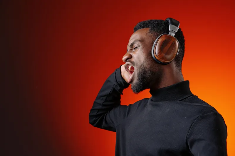 A young Black man passionately singing with headphones on, showcasing his emotions against a vibrant orange background, perfect for music related themes and concepts