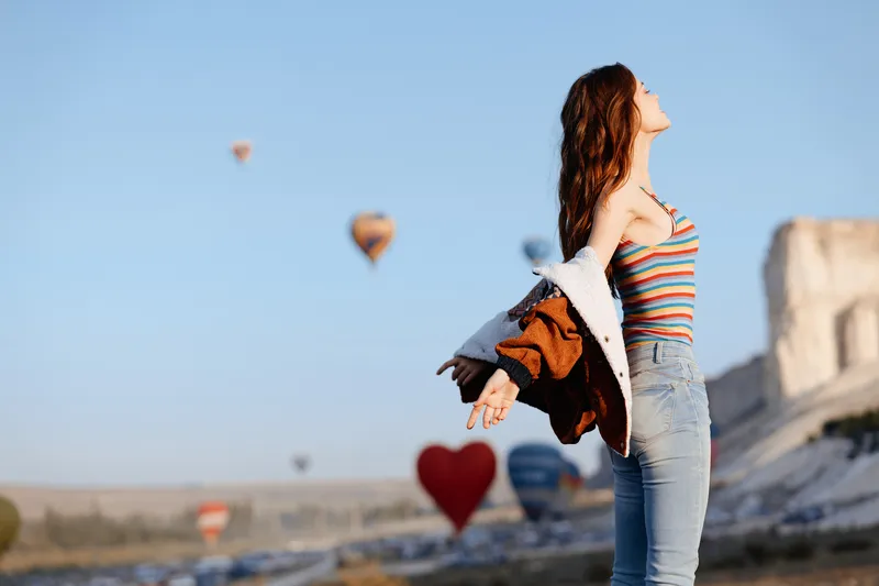 Взволнованная молодая женщина с раскинутыми руками стоит перед красочным воздушным шаром