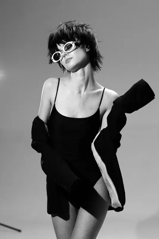 Black and white portrait of a stylish woman wearing sunglasses and a dark outfit with confident pose.