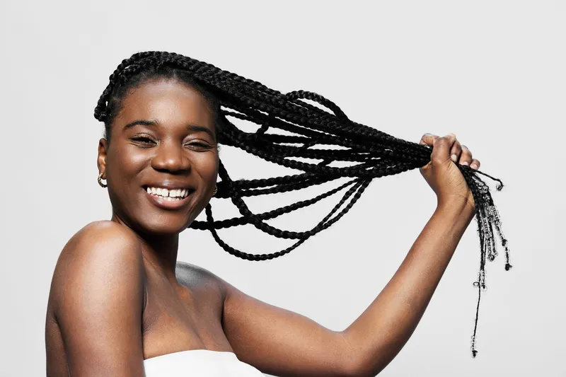 Smiling African woman showcasing long braided hair against a clean white background, capturing confidence and beauty in a vibrant style