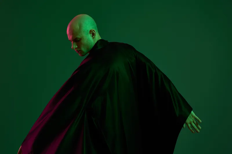 Mysterious man in a dark cloak, showcasing a dramatic pose against a green background, evoking intrigue and emotion, perfect for storytelling or artistic projects.