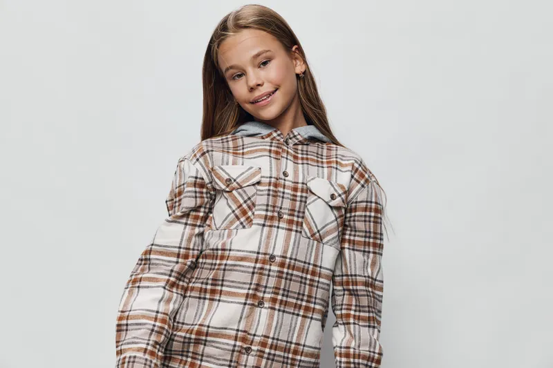 Girl with long hair wearing checkered shirt posing and smiling on white background, casual style, standing, looking away with slight head tilt, confident and happy.