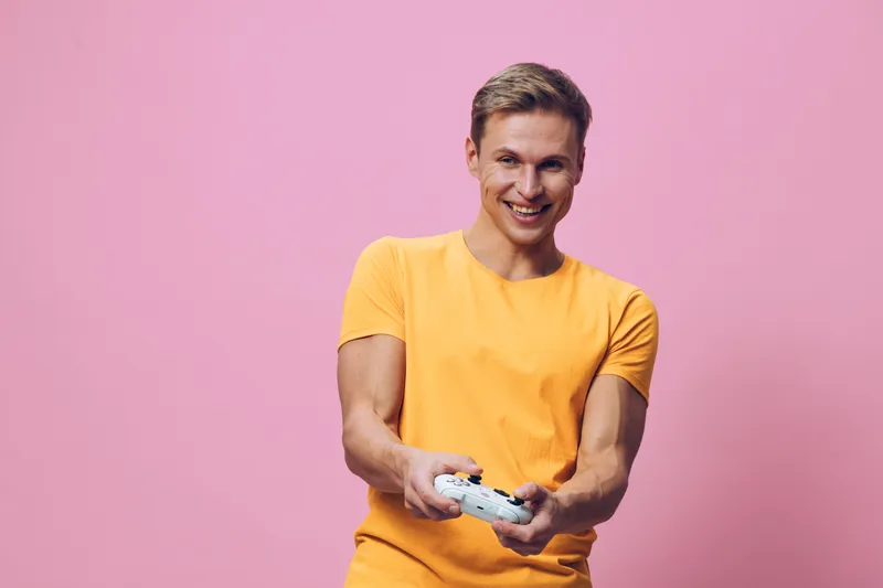 smiling young man wear yellow t-shirt play video game hold gamepad look camera isolated pink background digital entertainment concept