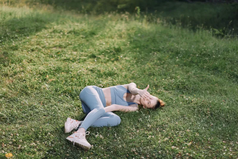 Young woman lying on the grass, enjoying a moment of relaxation in casual blue athletic wear, conveying a sense of peace and mindfulness in nature
