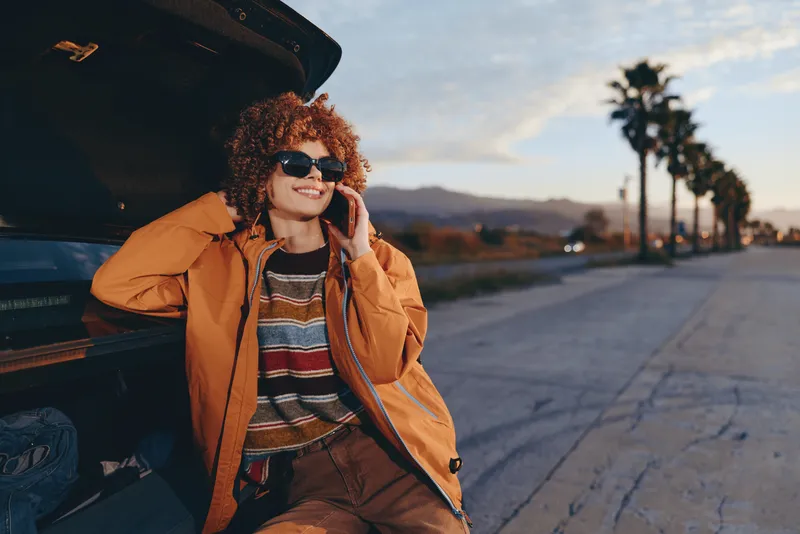 woman lifestyle, smiling, curly, sunglasses, jacket, outdoors, car, sunset, road, palm trees, golden sky, weekend casual vacation, portrait