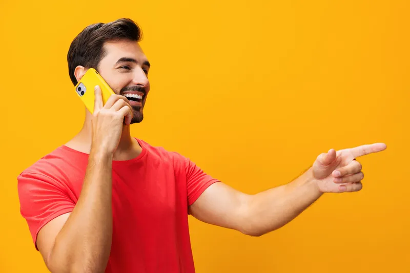 Мужчина в очках держит желтый смартфон, стоя в студии