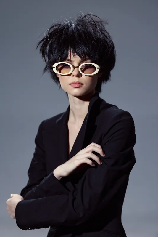 Stylish woman with short black hair wearing white round sunglasses and black blazer, modern fashion look