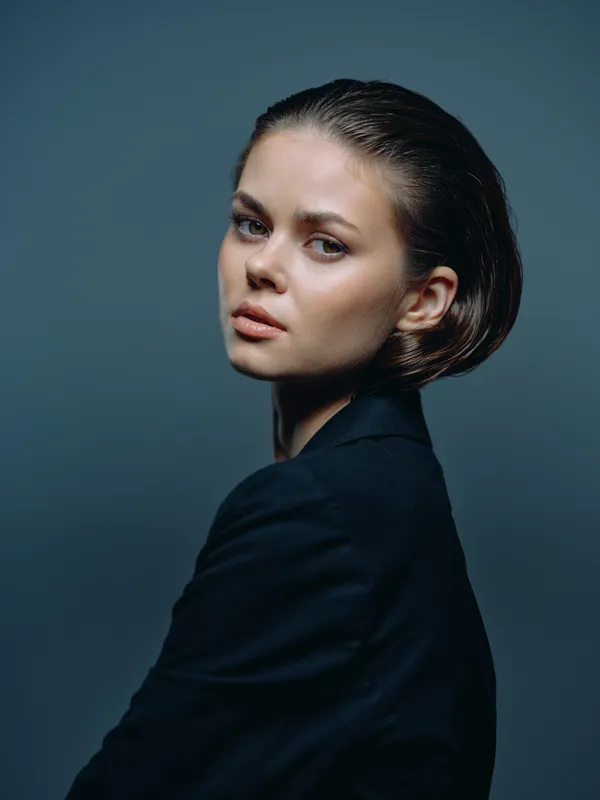 Portrait of a young woman with short hair wearing a black blazer against a dark background.