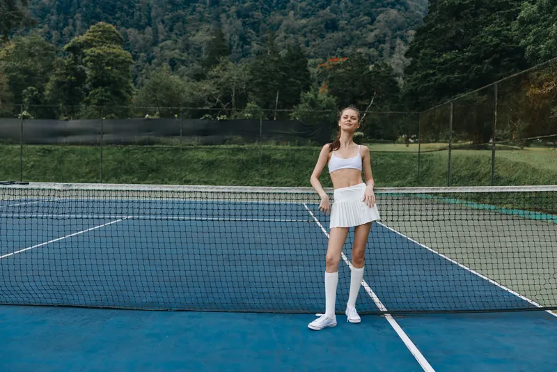 Athletic young woman in sporty outfit posing confidently on a tennis court surrounded by nature, showcasing a healthy lifestyle and active lifestyle choices