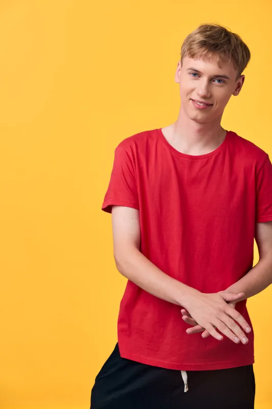 Young man wearing a red t shirt stands against a bright yellow background, casual fashion, relaxed pose, bold color contrast, lifestyle image highlighting youth energy and contemporary style