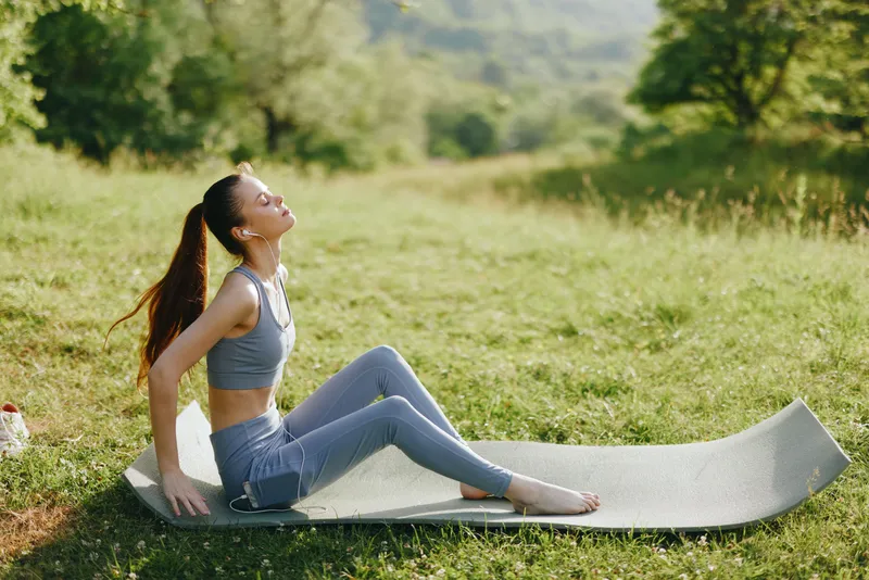 Young woman practicing yoga in nature, feeling calm and meditative during sunset with green surroundings while wearing comfortable activewear